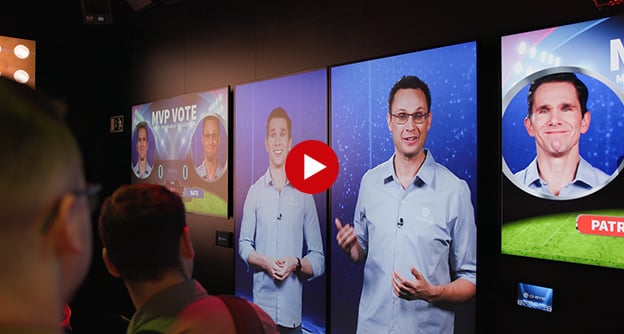 Q-SYSエンターテインメント＆ホスピタリティルームで、スクリーンにプレゼンテーションを行う従業員を表示したビデオサムネイル