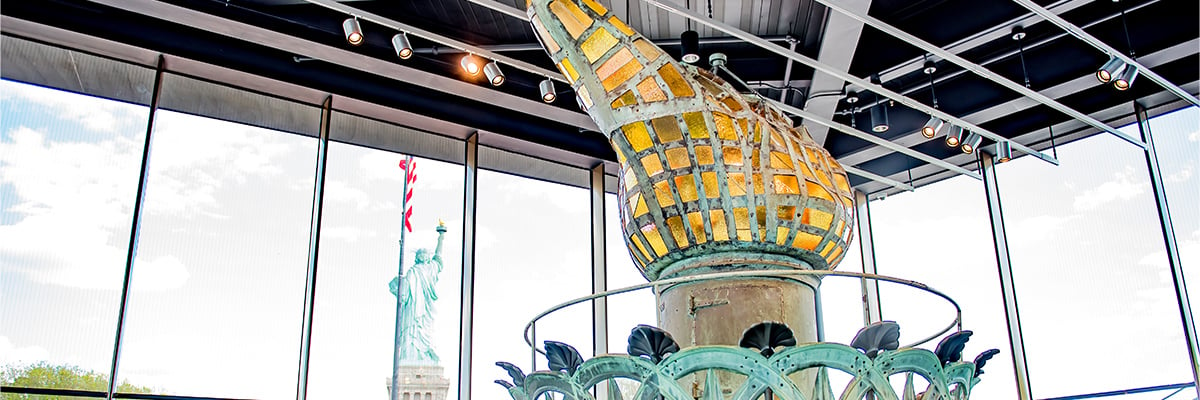 A model of the Statue of Liberty's torch with the back view of the Statue of Liberty in the background